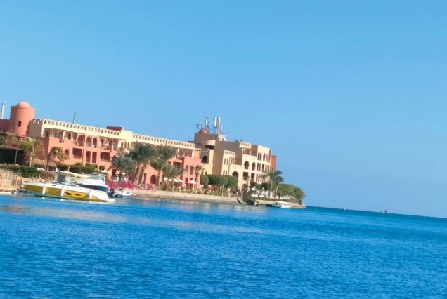 Das rosa und sandfarbene Ocean View Hotel in El Gouna mit Palmen und Bougainvillea direkt am Wasser, davor liegen kleine Motorboote
