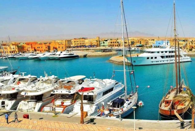Luxusyachten und ein hölzernes Segelschiff im Yachthafen von El Gouna, dahinter bunte Gebäude und die Berge am Roten Meer