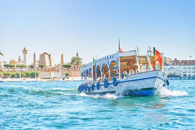 Buntes Ausflugsboot auf dem Nil vor der Kulisse der Tempel von Luxor